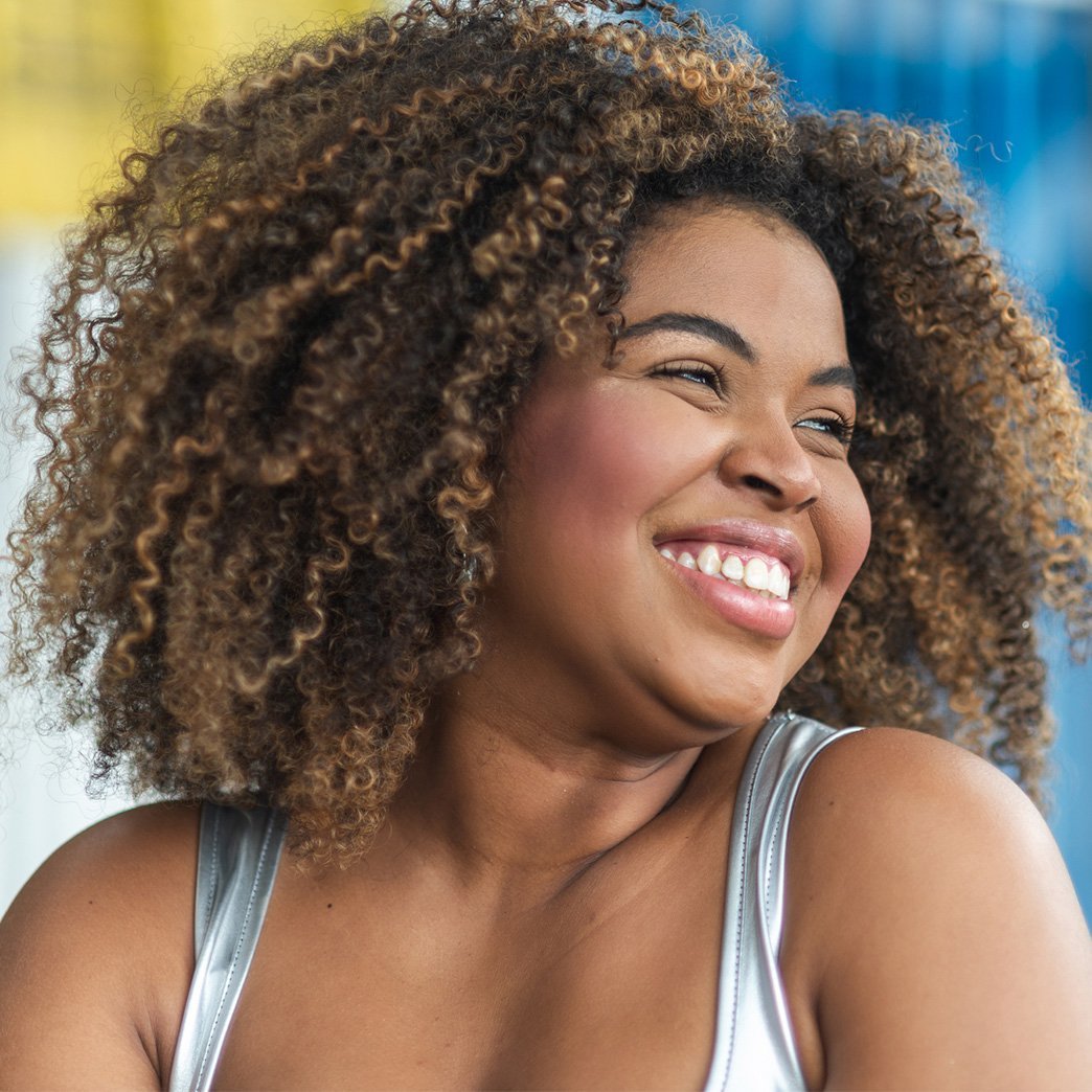 Portrait of young woman with 4A curls looking to the side, smiling.